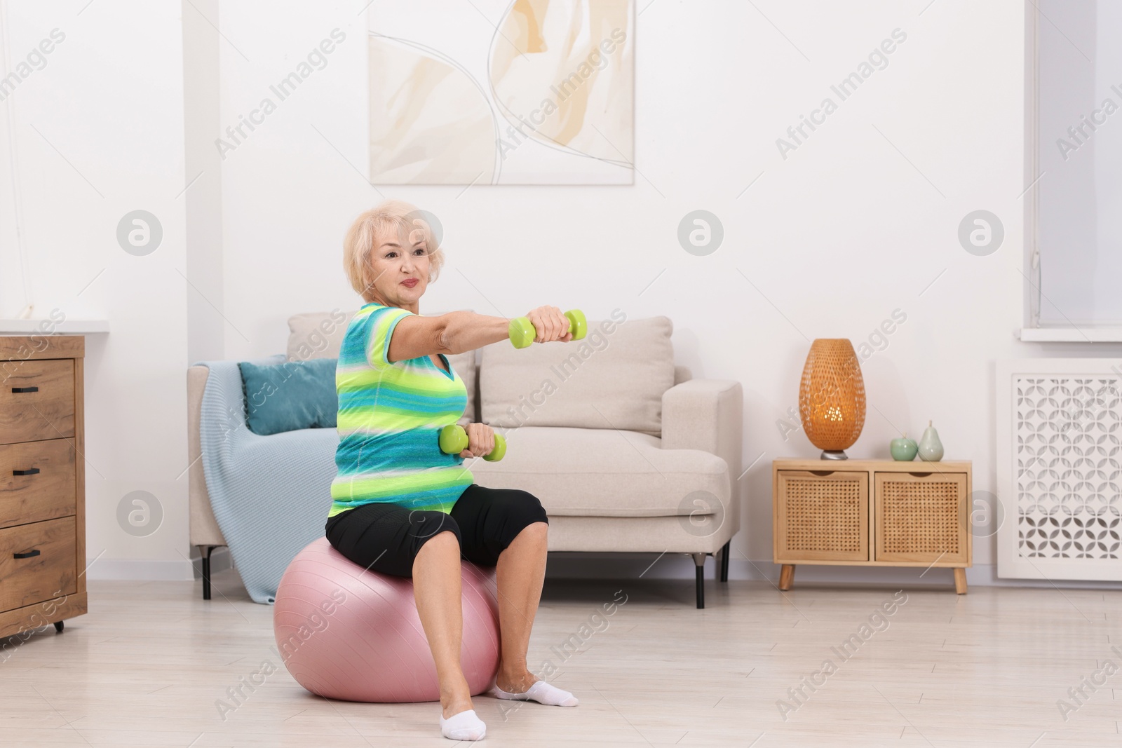 Photo of Senior woman exercising with fitness ball and dumbbells at home, space for text