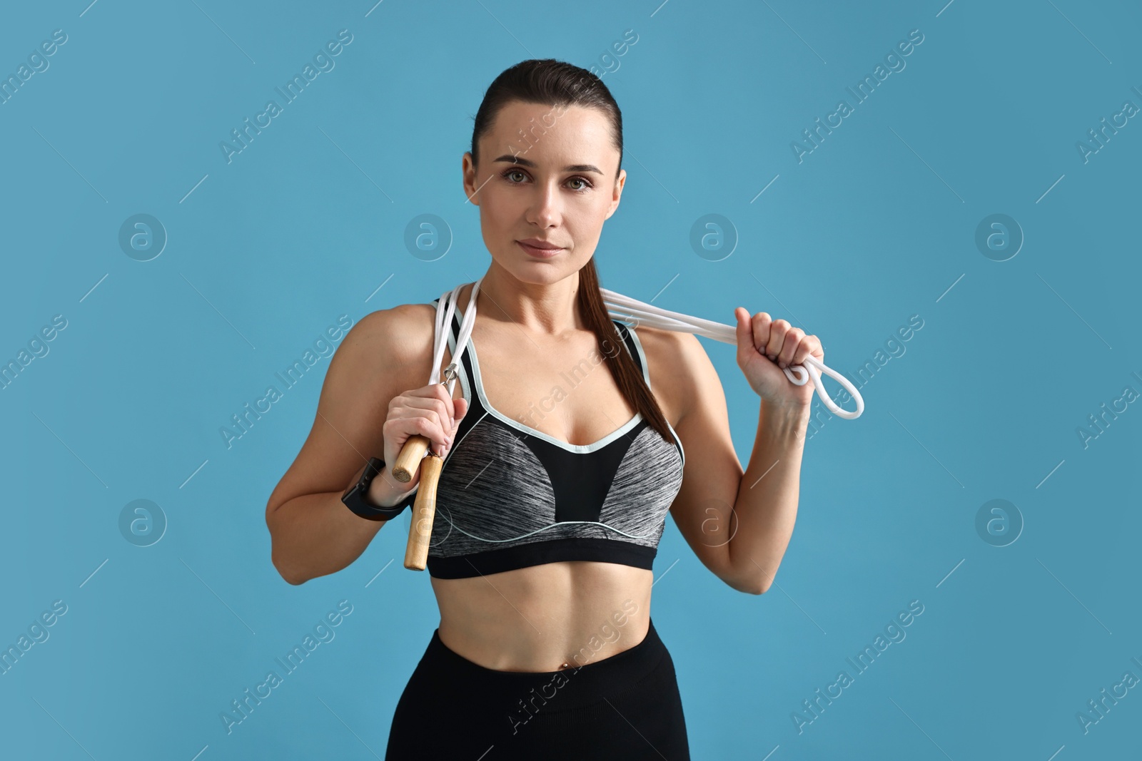 Photo of Woman in gym clothes with skipping rope on light blue background