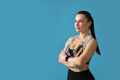 Photo of Woman in gym clothes with skipping rope on light blue background, space for text