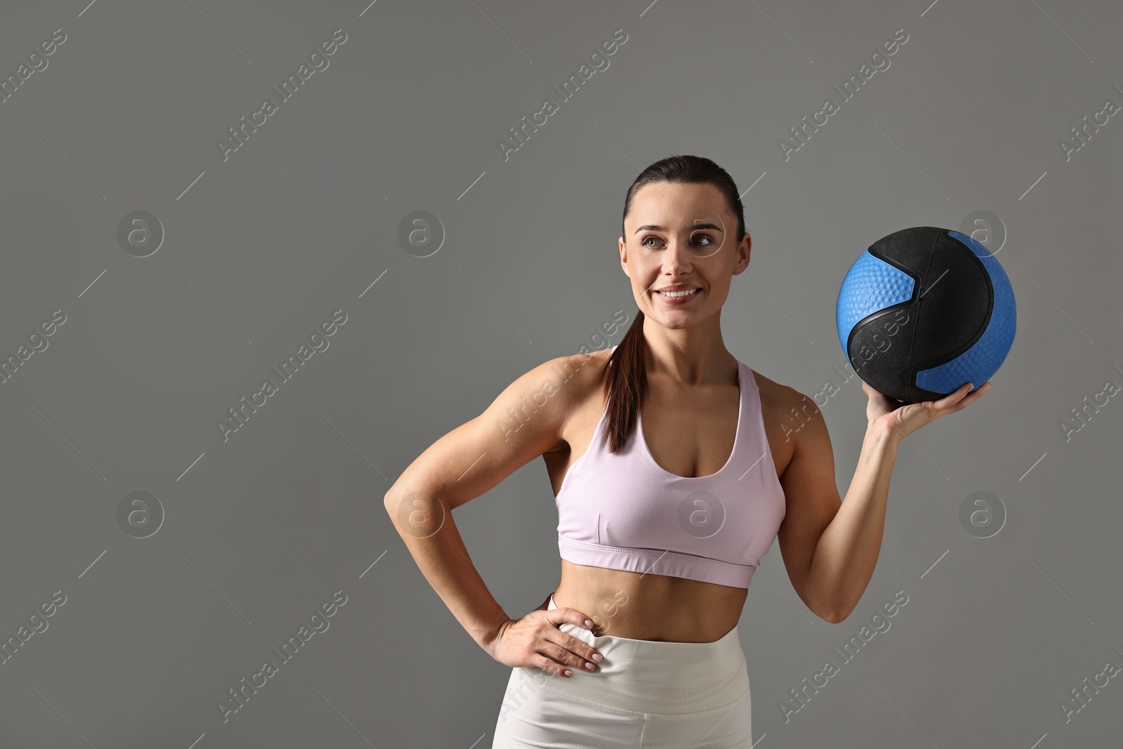 Photo of Woman in gym clothes doing exercise with medicine ball on grey background, space for text