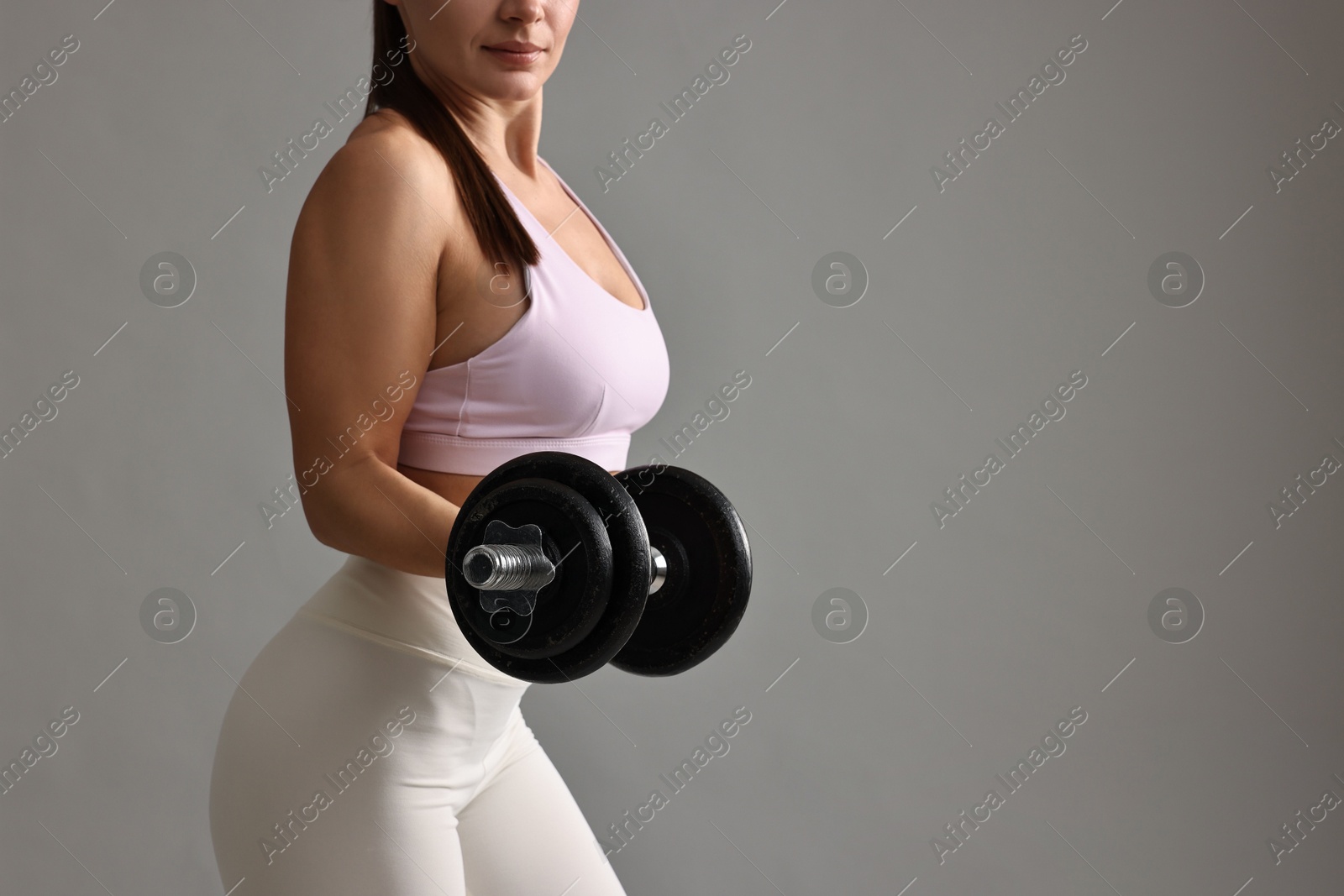 Photo of Woman in gym clothes exercising with barbell on grey background, closeup. Space for text