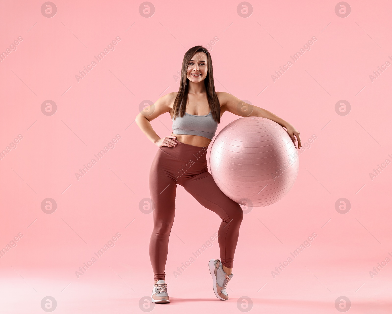 Photo of Woman in gym clothes with fitness ball on pink background