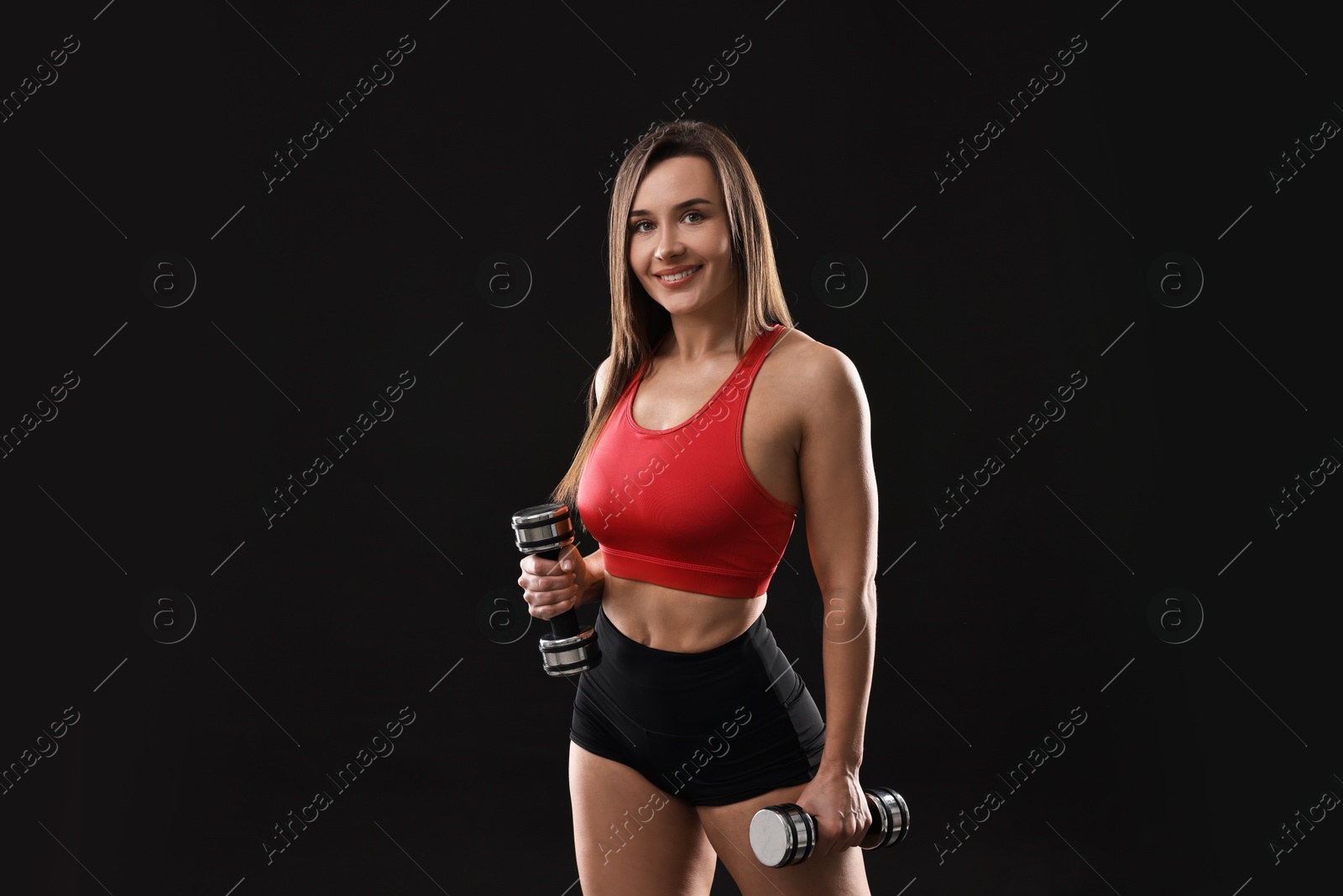 Photo of Woman in gym clothes exercising with dumbbells on black background