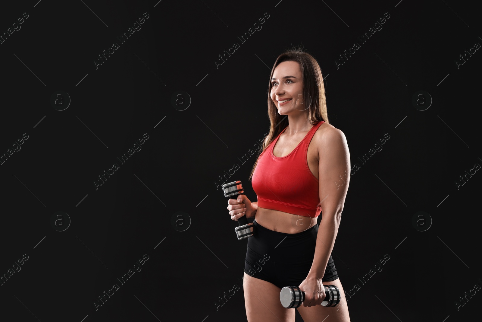 Photo of Woman in gym clothes exercising with dumbbells on black background, space for text