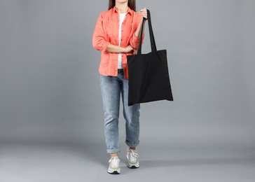 Photo of Woman with blank black shopper bag on grey background, closeup. Mockup for design