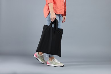 Photo of Woman with blank black shopper bag on grey background, closeup. Mockup for design