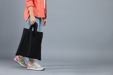 Photo of Woman with blank black shopper bag on grey background, closeup. Mockup for design