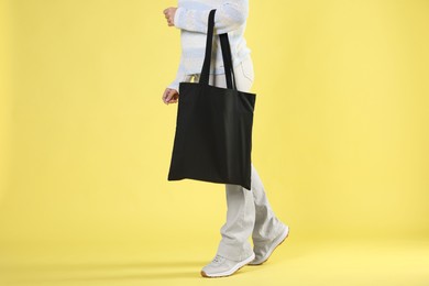 Photo of Woman with blank black shopper bag on yellow background, closeup. Mockup for design