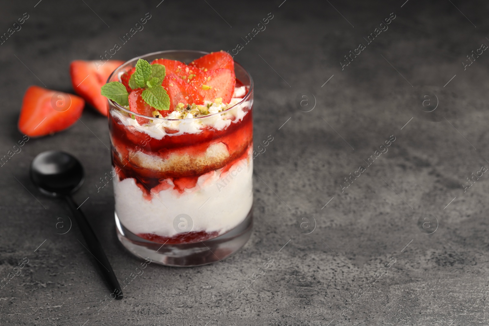 Photo of Tasty trifle dessert. Strawberries, sponge cake and whipped cream in glass on grey table, space for text