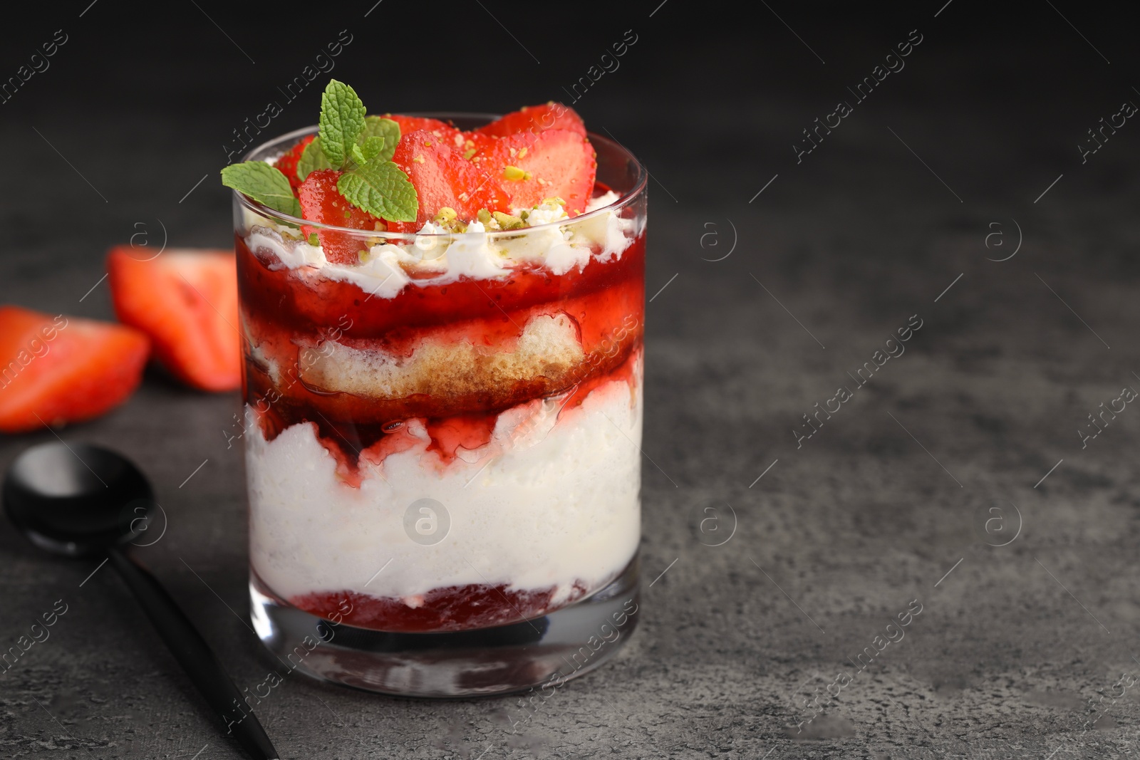 Photo of Tasty trifle dessert. Strawberries, sponge cake and whipped cream in glass on grey table, space for text