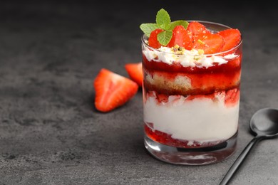 Photo of Tasty trifle dessert. Strawberries, sponge cake and whipped cream in glass on grey table, space for text