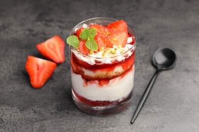 Photo of Tasty trifle dessert. Strawberries, sponge cake and whipped cream in glass on grey table