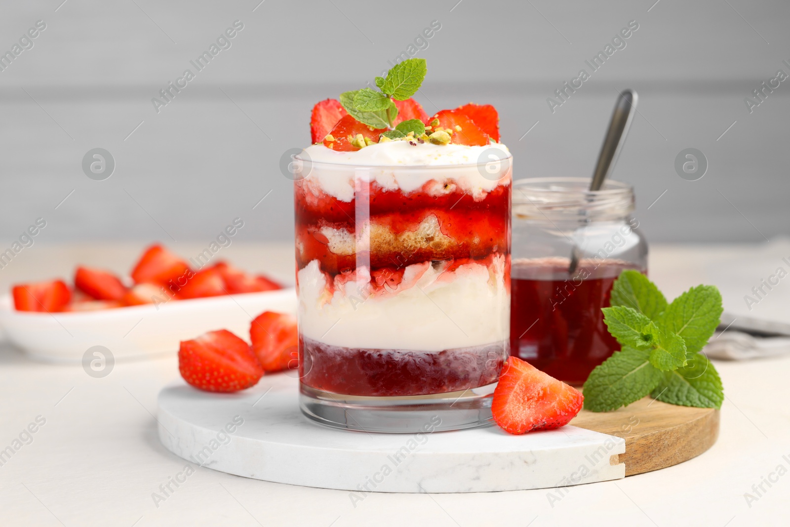 Photo of Tasty trifle dessert. Strawberries, sponge cake and whipped cream in glass on beige table