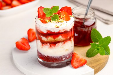 Photo of Tasty trifle dessert. Strawberries, sponge cake and whipped cream in glass on beige table