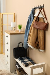 Photo of Coat rack with clothes, mirror, shoe storage bench and chest of drawers in hallway. Interior design