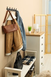 Photo of Coat rack with clothes, mirror, shoe storage bench and chest of drawers in hallway. Interior design