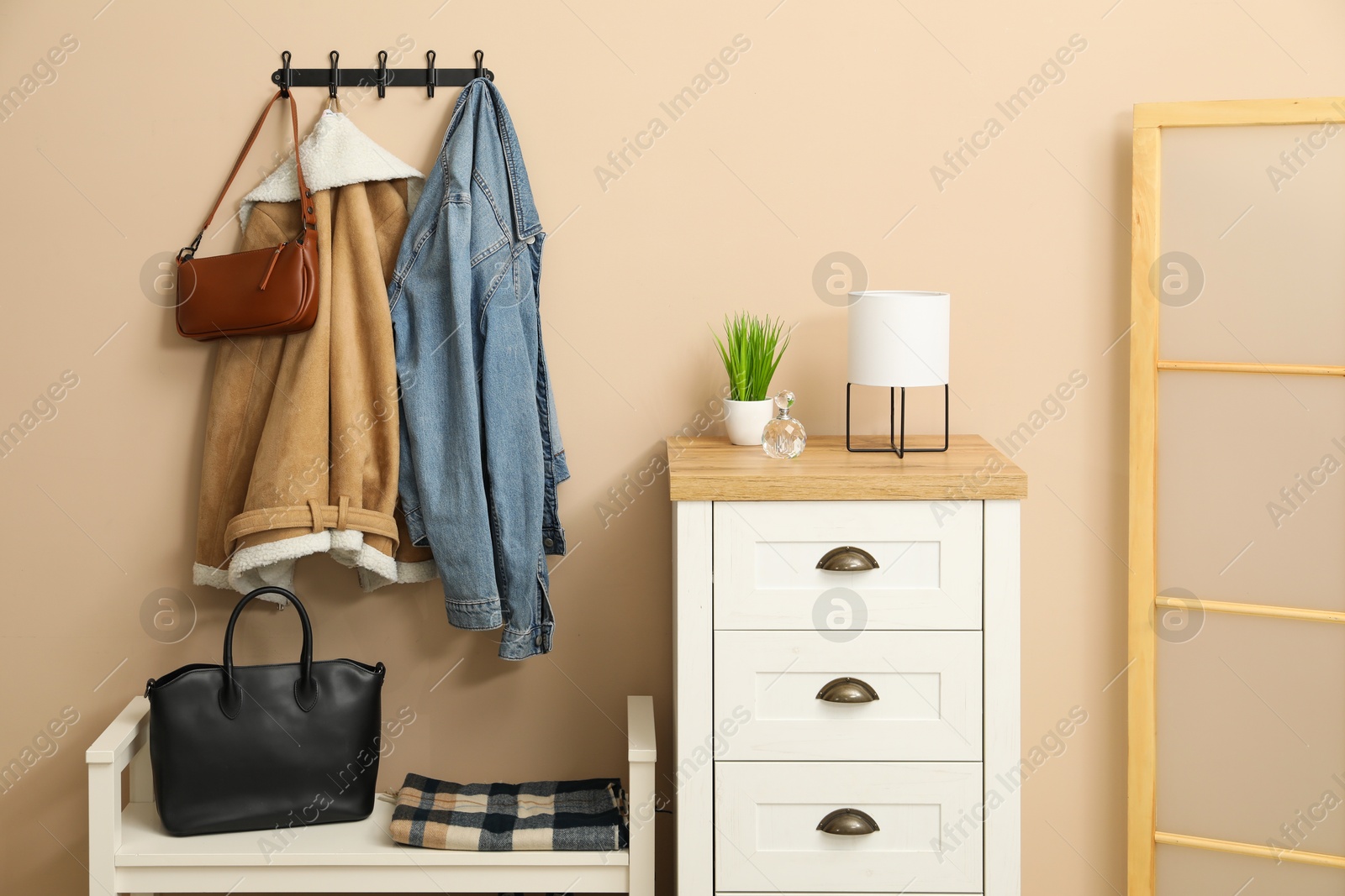 Photo of Coat rack with clothes, mirror, shoe storage bench and chest of drawers in hallway. Interior design