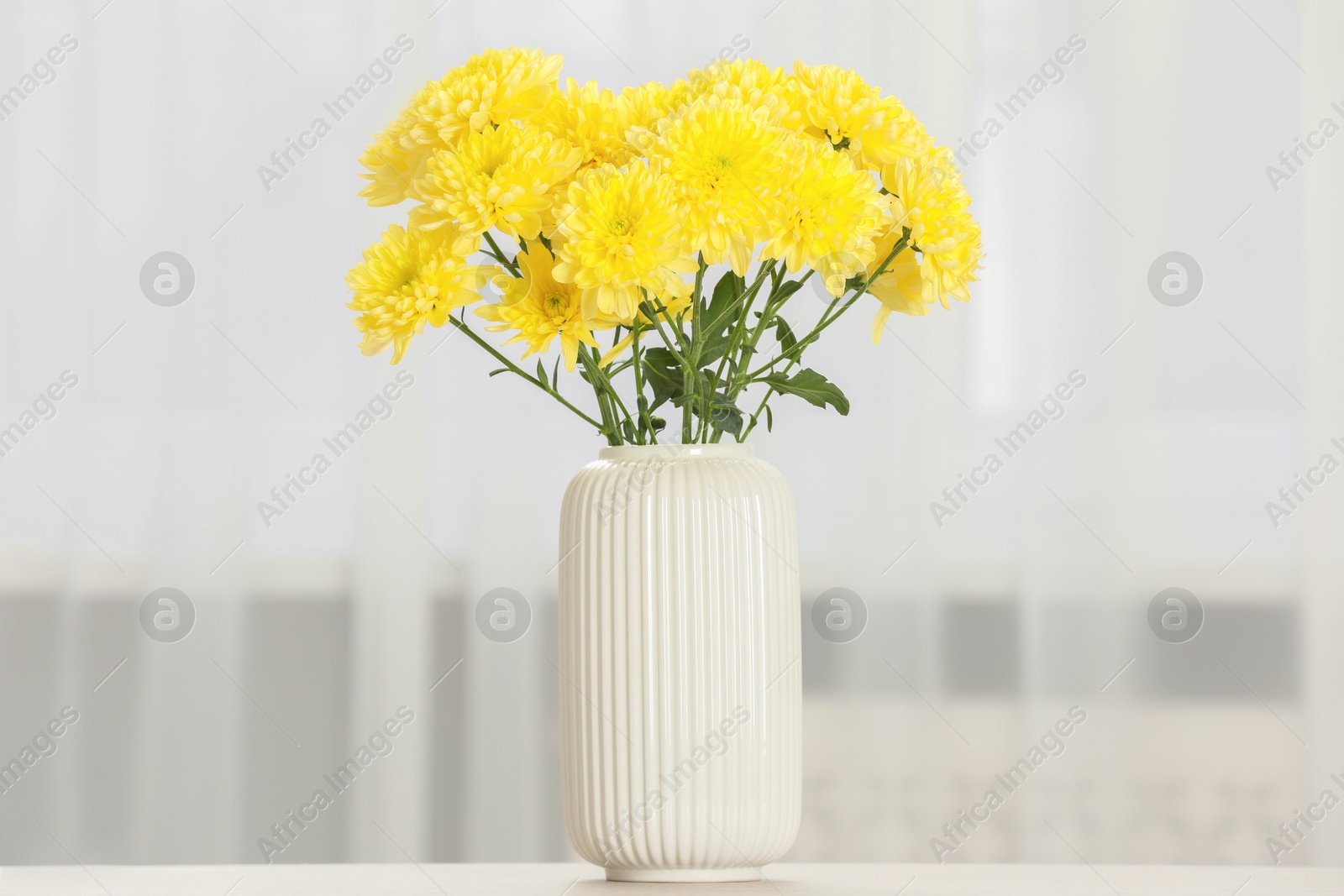 Photo of Beautiful yellow flowers in vase on table at home