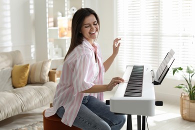 Photo of Smiling woman playing synthesizer at home. Electronic musical instrument