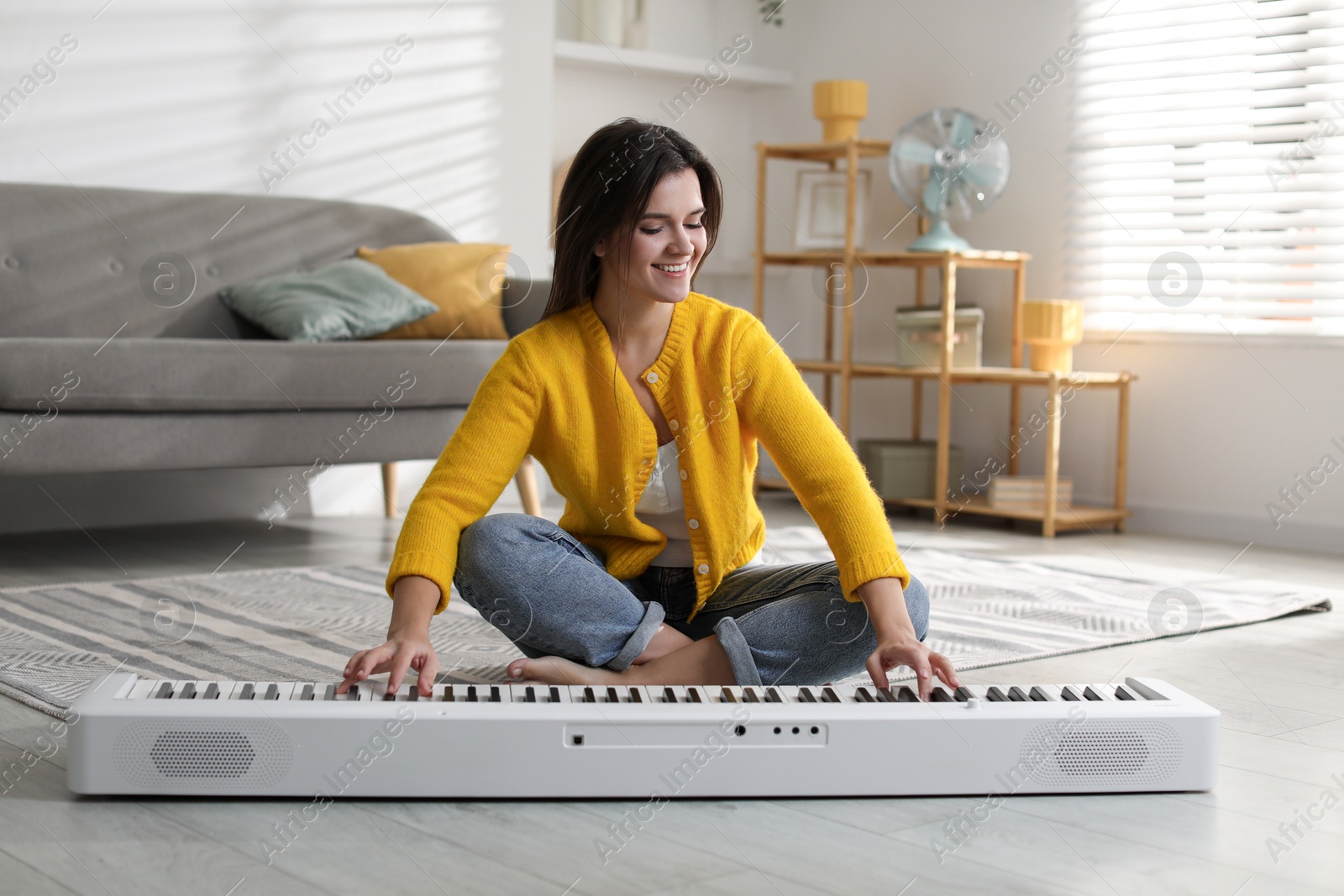 Photo of Smiling woman playing synthesizer on floor at home