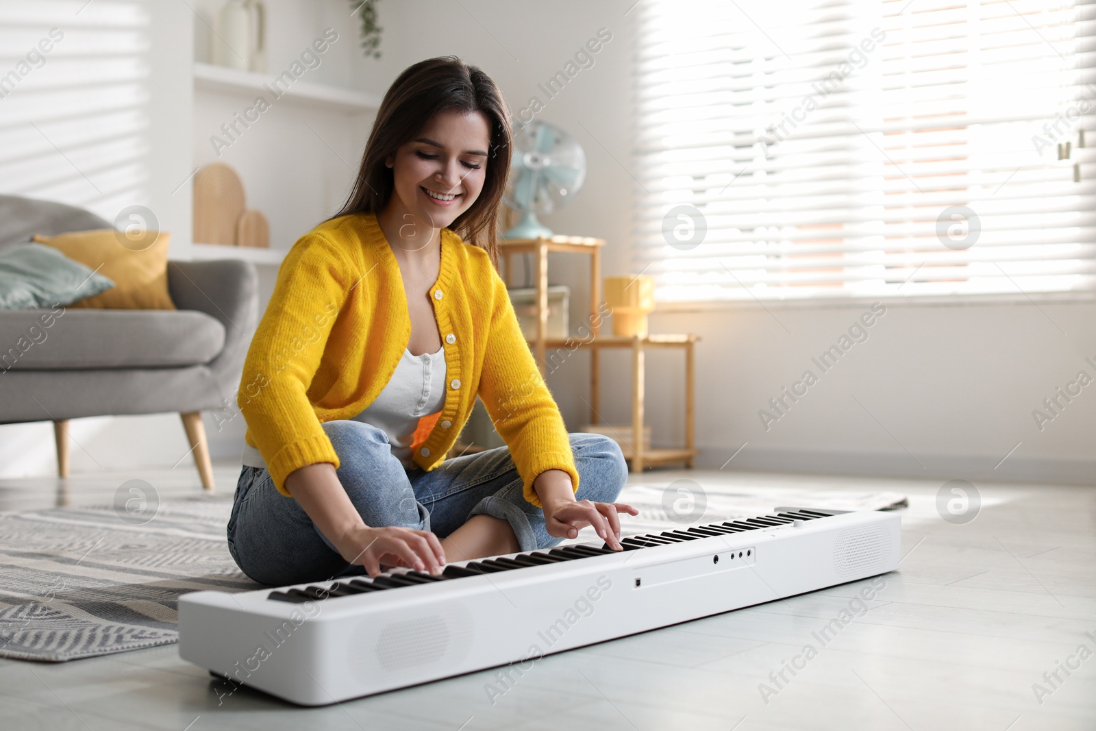 Photo of Smiling woman playing synthesizer on floor at home