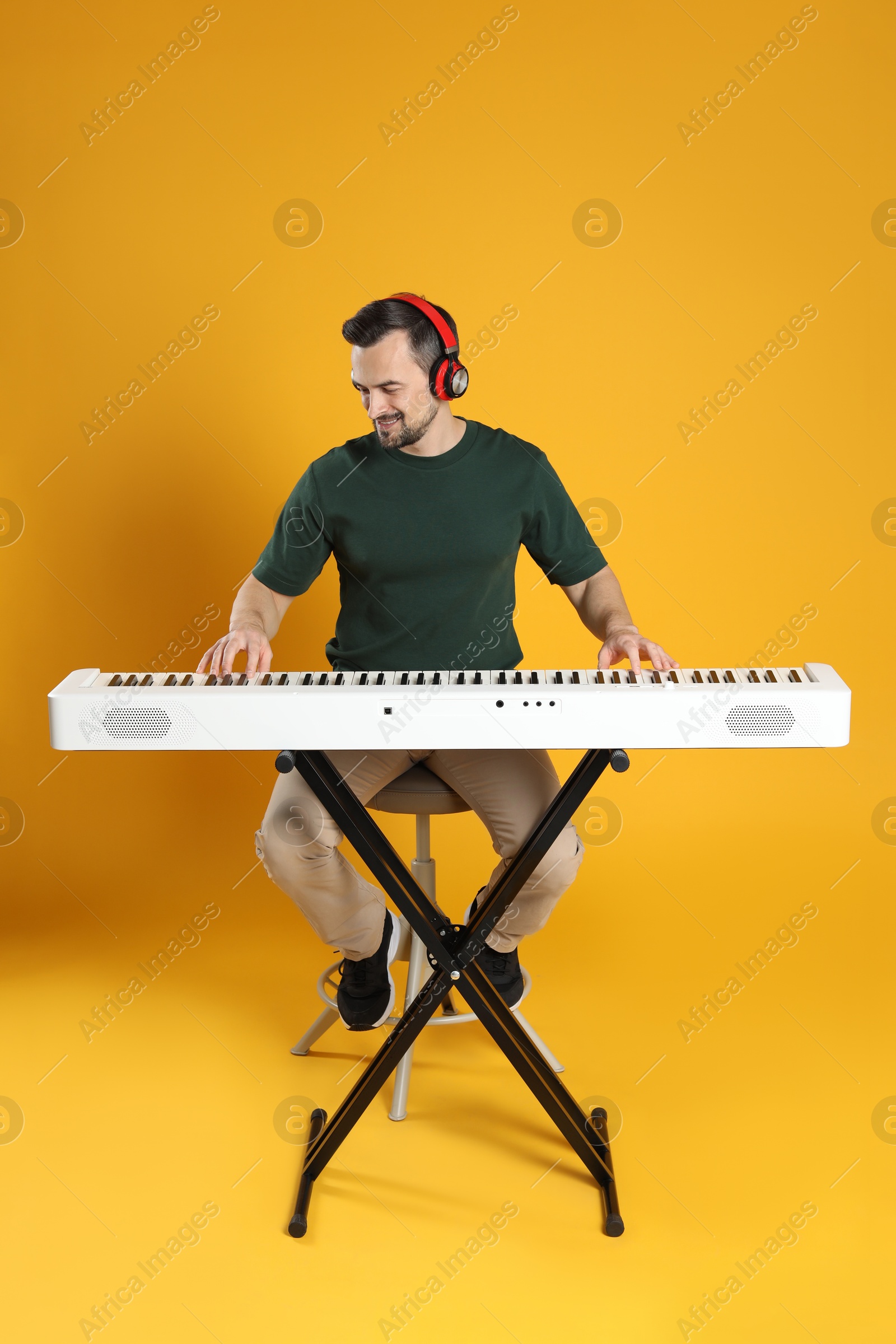 Photo of Smiling man in headphones playing synthesizer on orange background