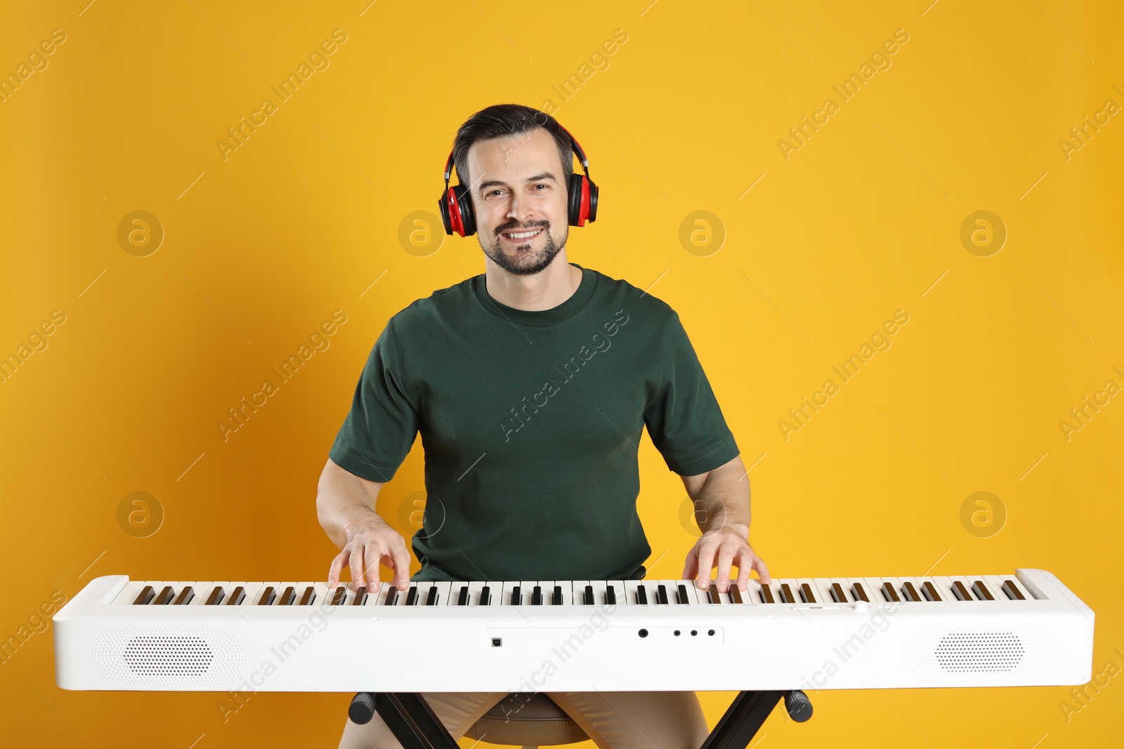 Photo of Smiling man in headphones playing synthesizer on orange background