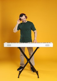 Photo of Man in headphones playing synthesizer on orange background