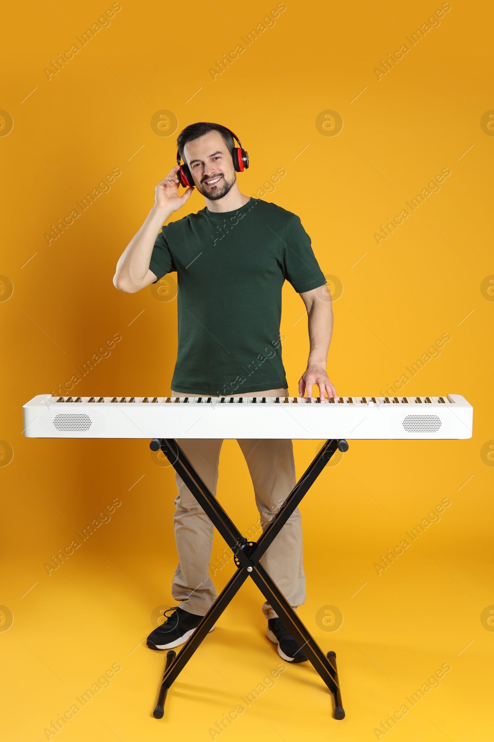 Photo of Smiling man in headphones playing synthesizer on orange background