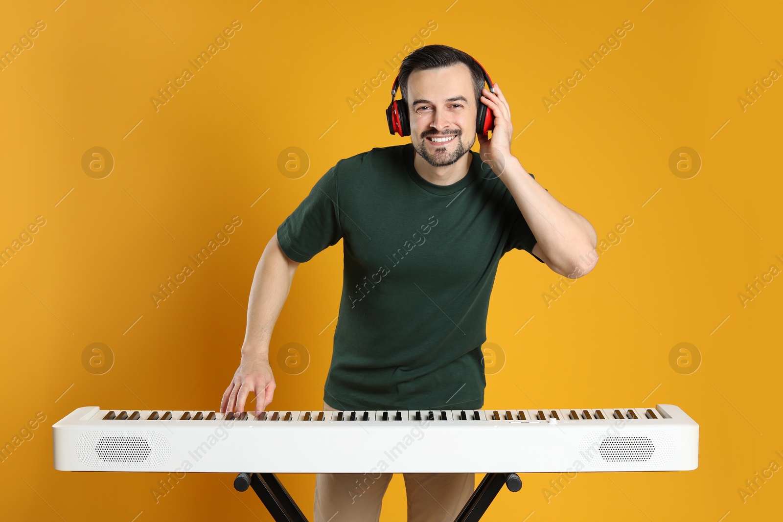 Photo of Smiling man in headphones playing synthesizer on orange background