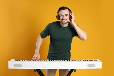 Photo of Smiling man in headphones playing synthesizer on orange background