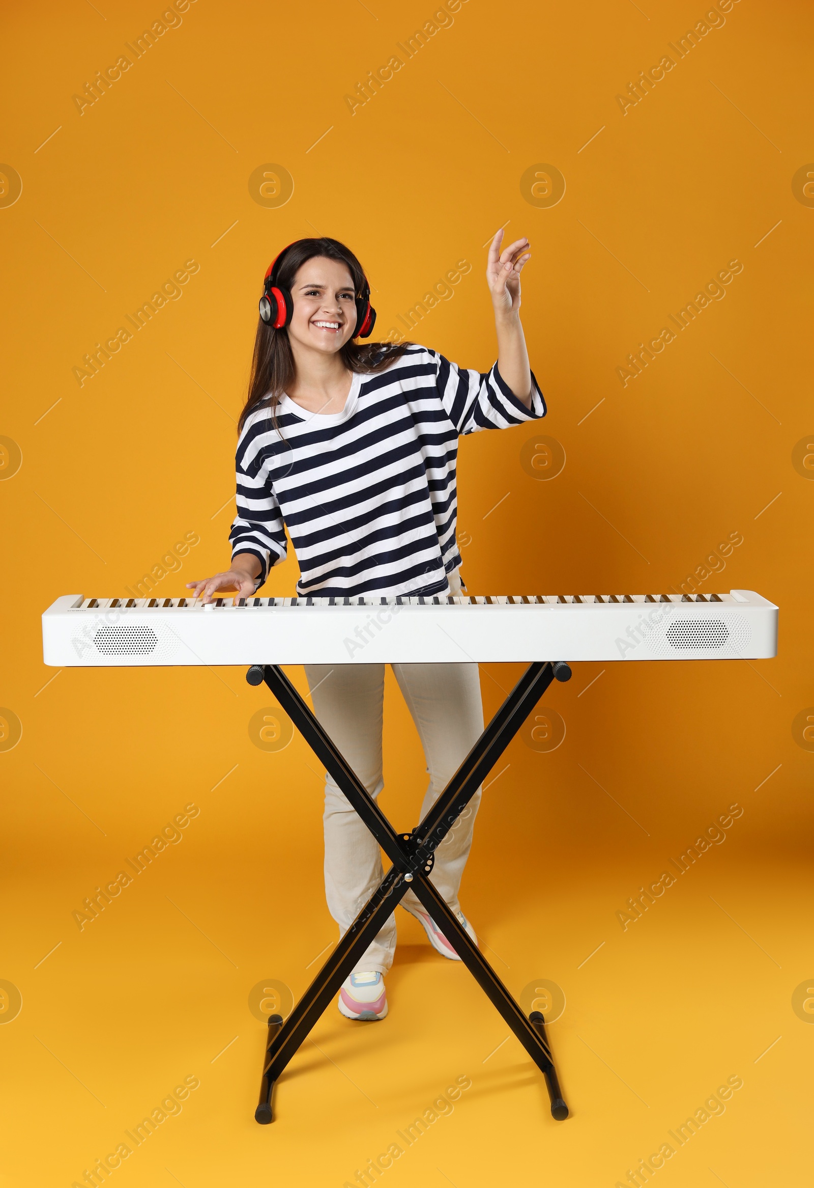 Photo of Smiling woman in headphones playing synthesizer on orange background