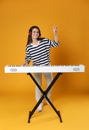 Photo of Smiling woman in headphones playing synthesizer on orange background