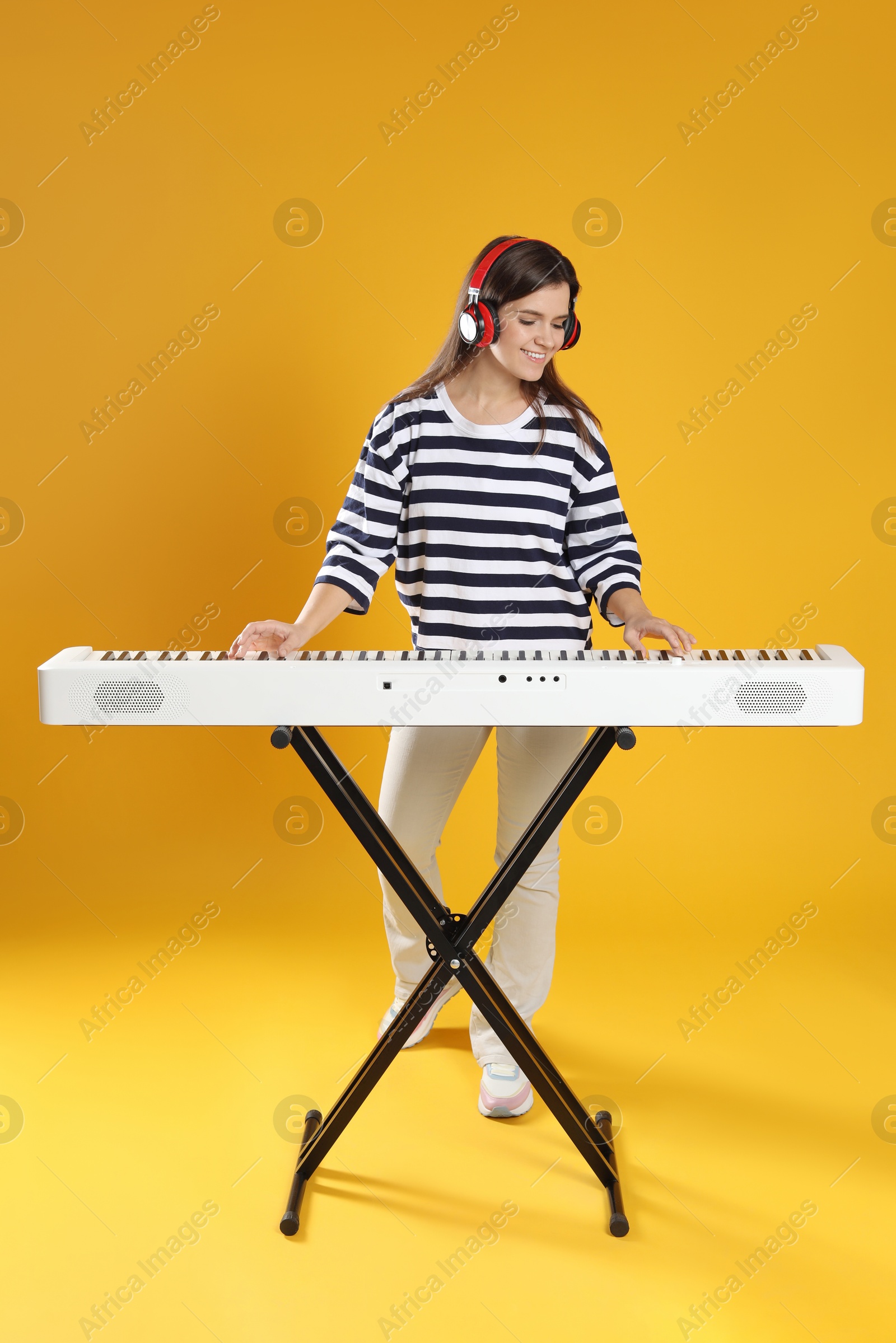 Photo of Smiling woman in headphones playing synthesizer on orange background