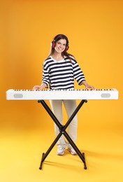 Photo of Smiling woman in headphones playing synthesizer on orange background