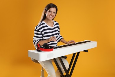 Photo of Smiling woman playing synthesizer on orange background