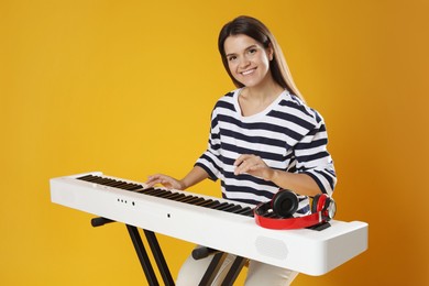 Photo of Smiling woman playing synthesizer on orange background