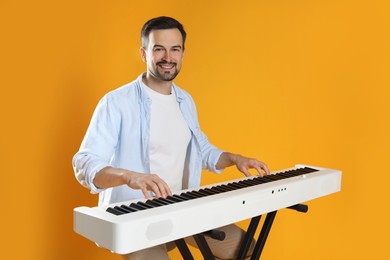 Photo of Smiling man playing synthesizer on orange background