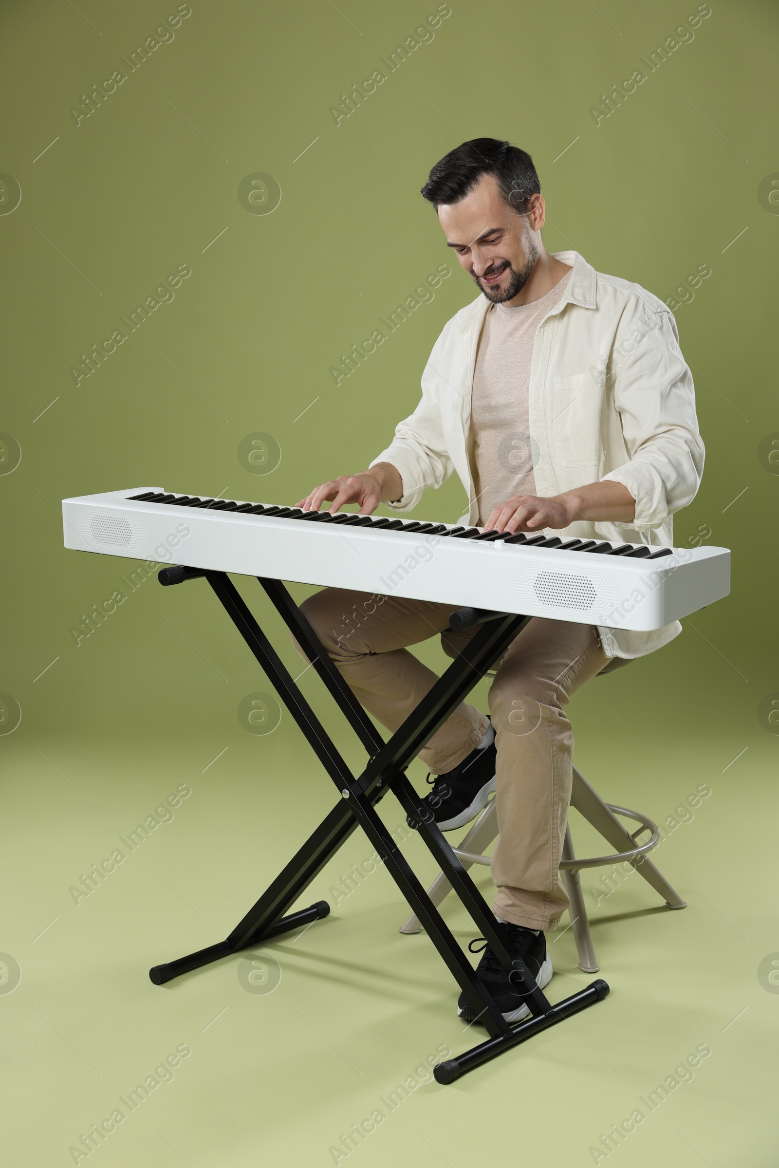 Photo of Smiling man playing synthesizer on olive background