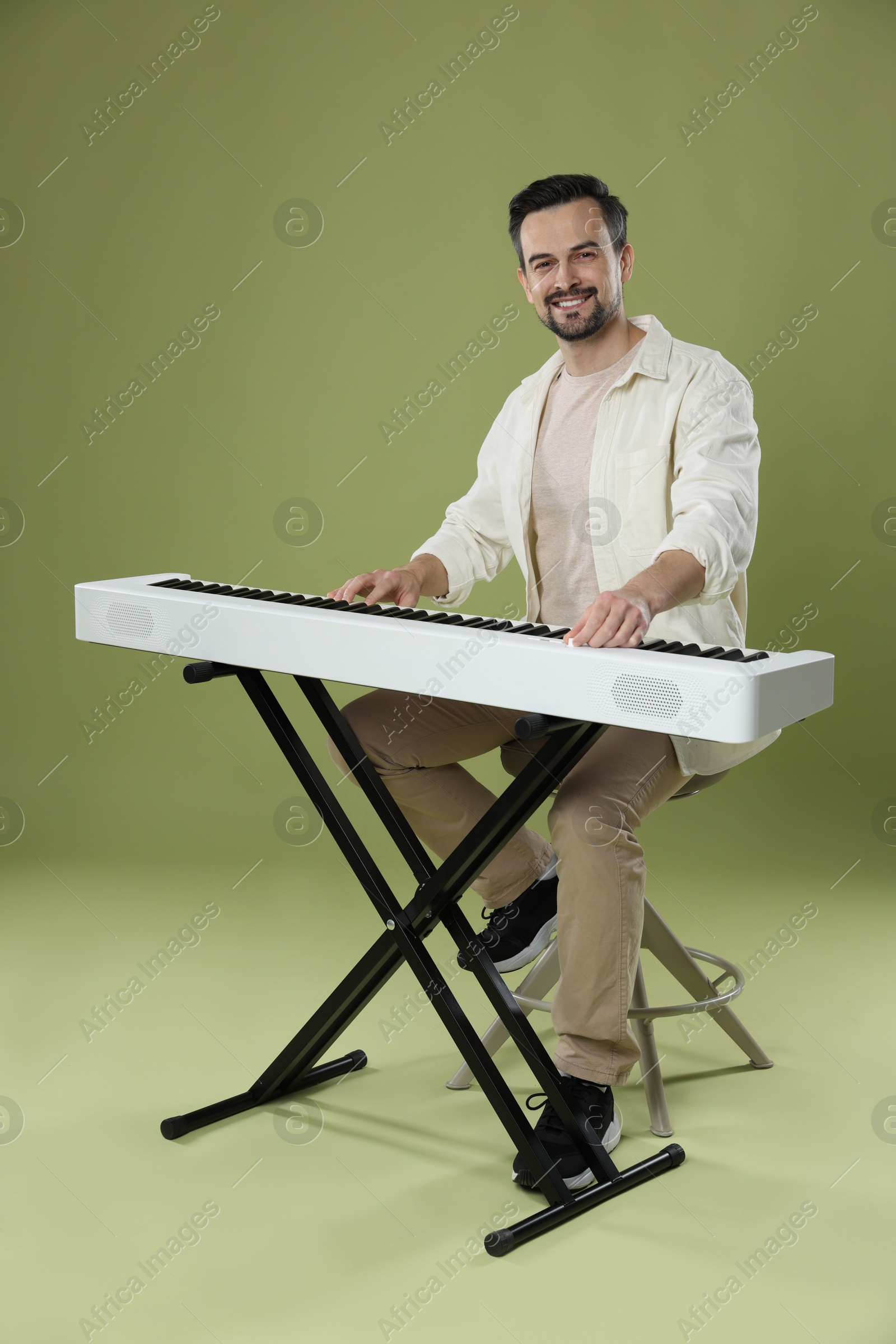 Photo of Smiling man playing synthesizer on olive background