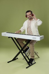 Photo of Smiling man in headphones playing synthesizer on olive background