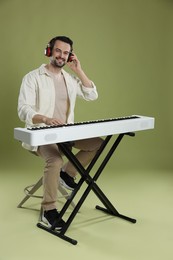 Photo of Smiling man in headphones playing synthesizer on olive background