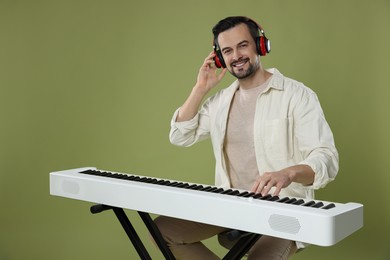 Photo of Smiling man in headphones playing synthesizer on olive background