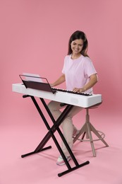 Photo of Smiling woman playing synthesizer on pink background