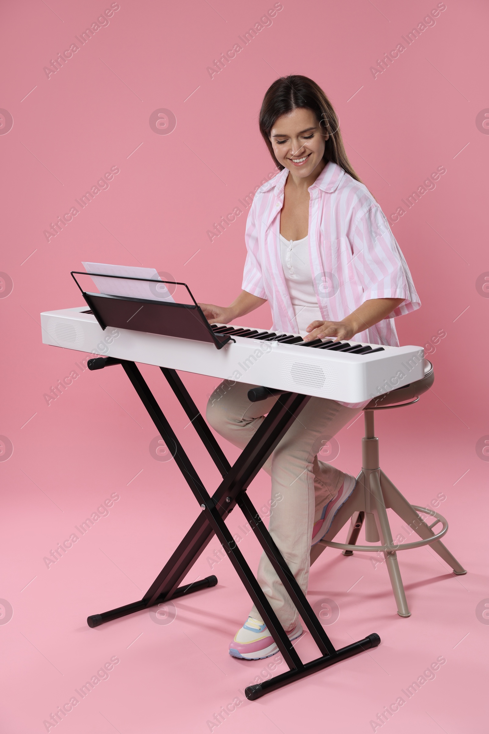 Photo of Smiling woman playing synthesizer on pink background