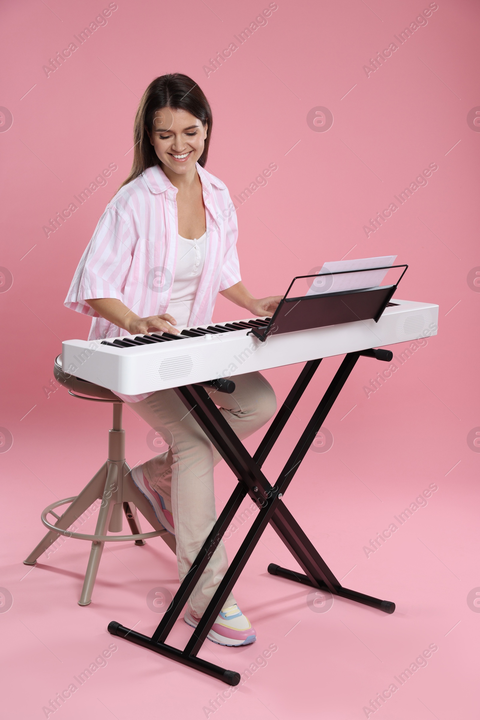 Photo of Smiling woman playing synthesizer on pink background