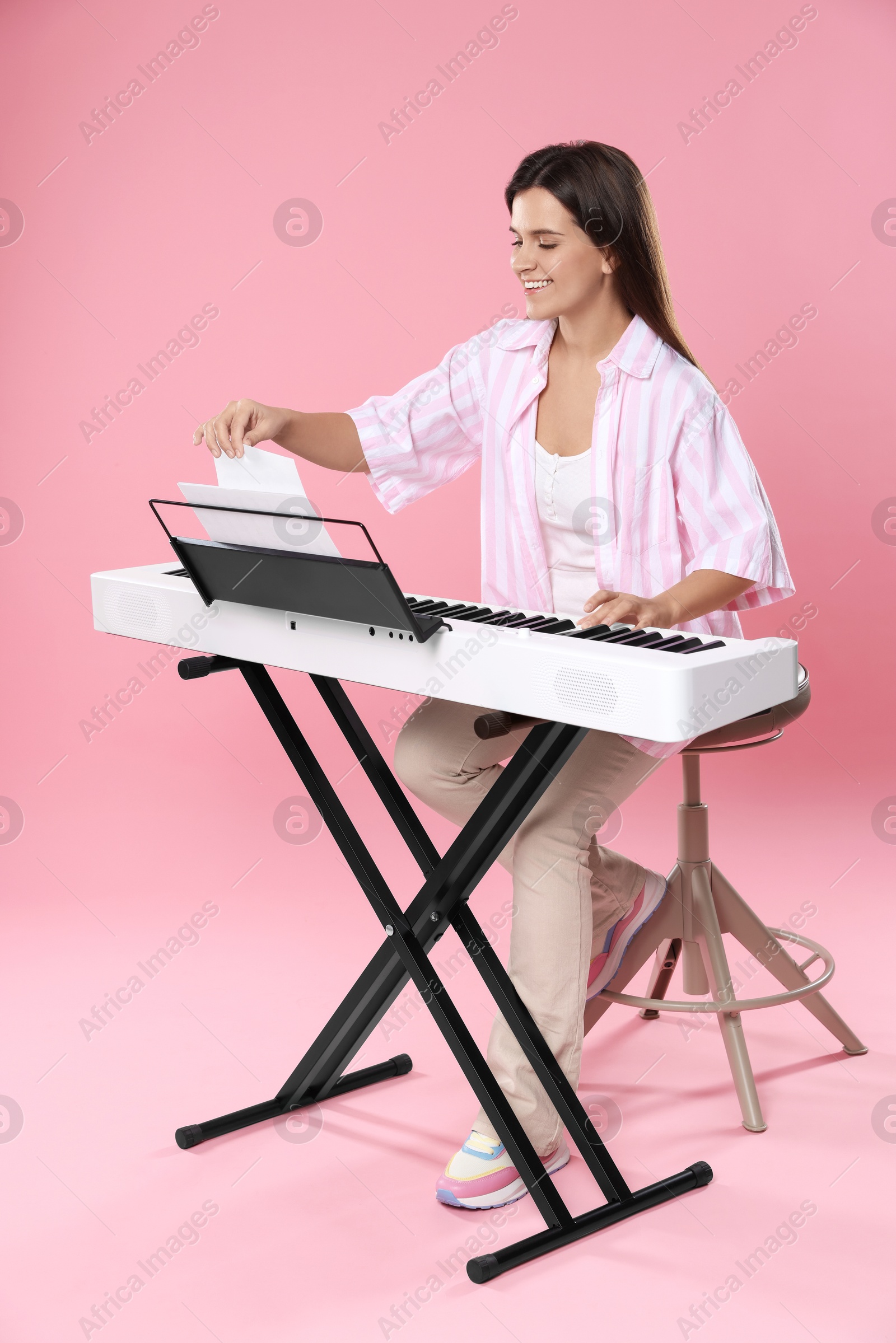 Photo of Smiling woman playing synthesizer on pink background