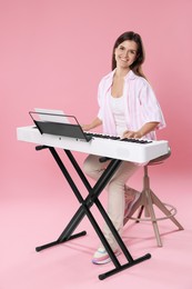 Photo of Smiling woman playing synthesizer on pink background