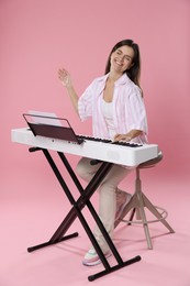 Photo of Smiling woman playing synthesizer on pink background