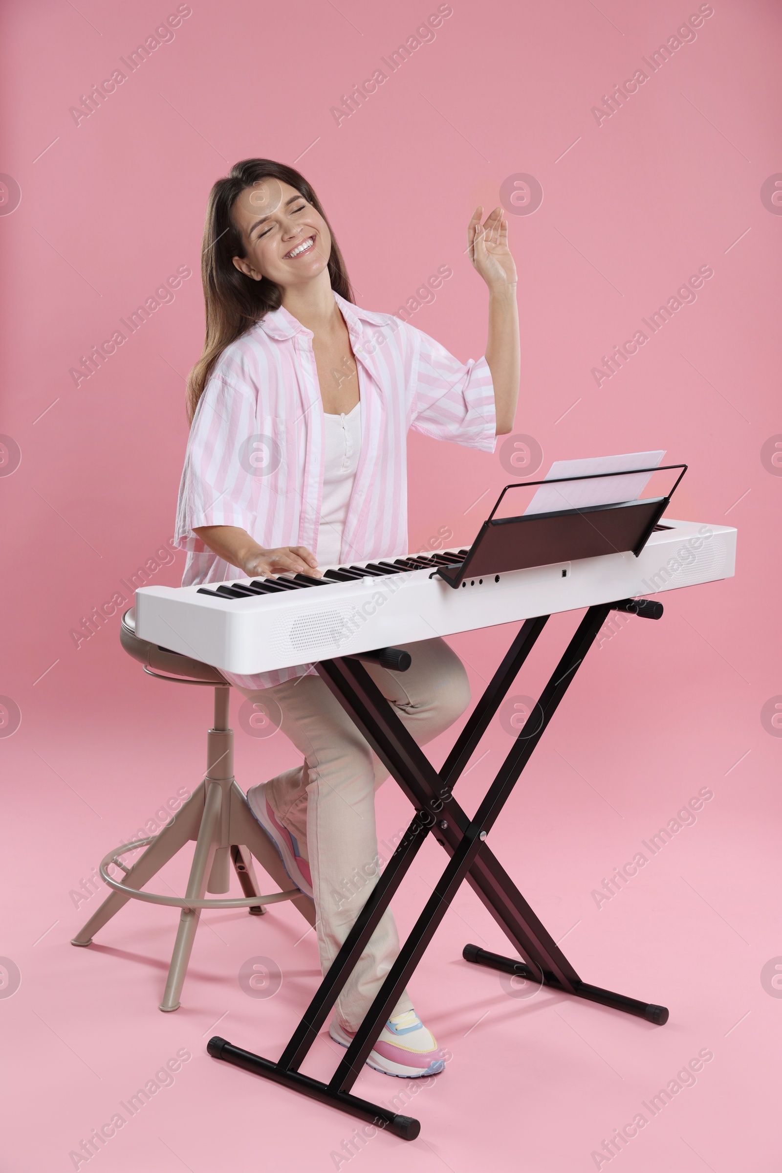 Photo of Smiling woman playing synthesizer on pink background